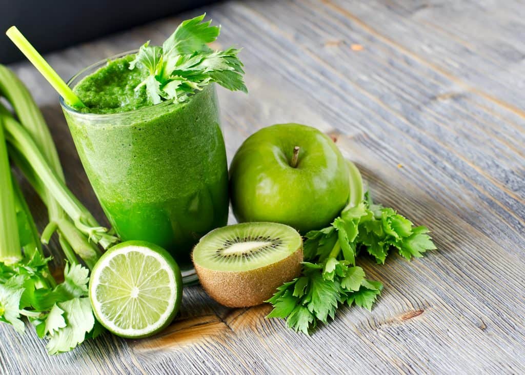 green smoothie in glass with straw on wood background