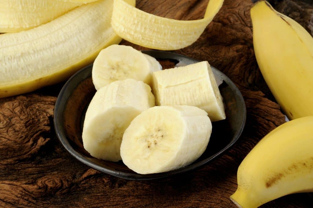 sliced banana in bowl on dark wooden background