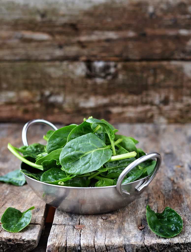 spinach in metal bowl with wooden background