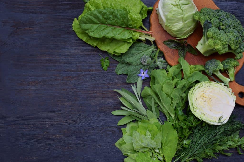 Composition on a dark background of green leafy vegetables containing folic acid, riboflavin, vitamin B9, B2, K, C - cabbage broccoli, chard, lettuce, spinach, parsley and celery, dill, sage. Flat lay