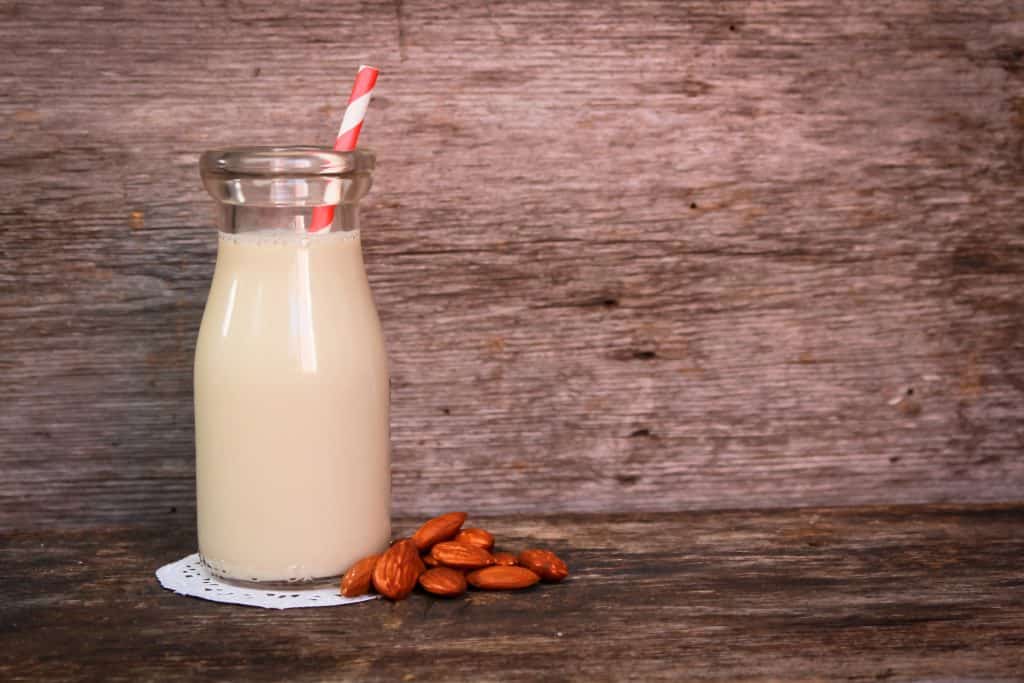 fresh almond milk in a glass jar on wooden background with almonds