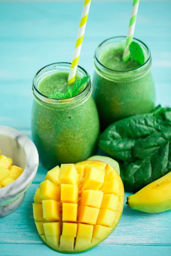 mango and spinach smoothie with bananas in glasses with straws