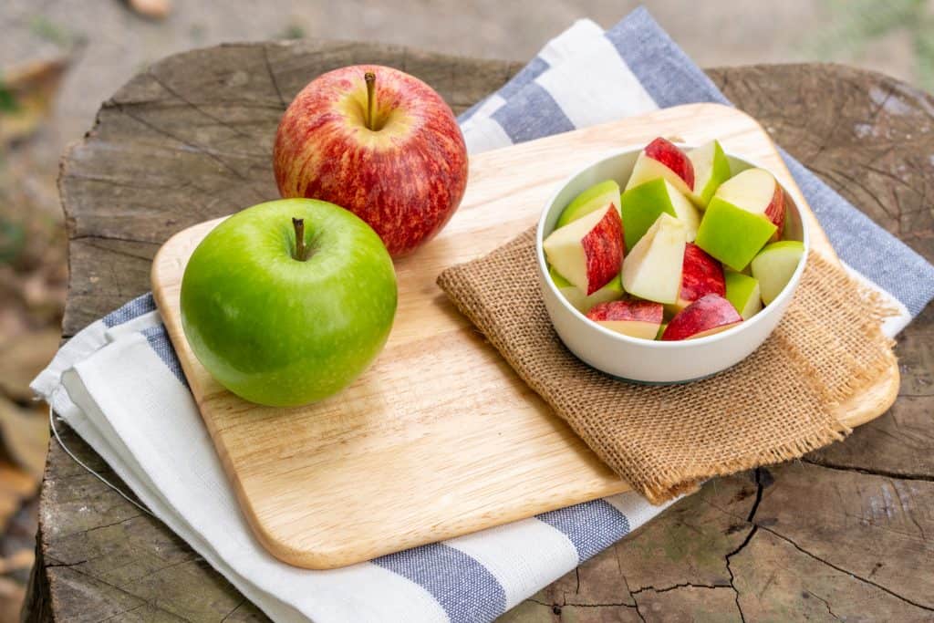 red and green apples and slices on wooden background