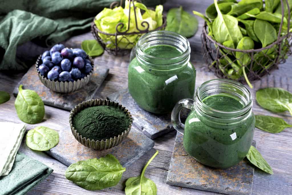 green smoothies surrounded by leafy greens, blueberries and greens powder