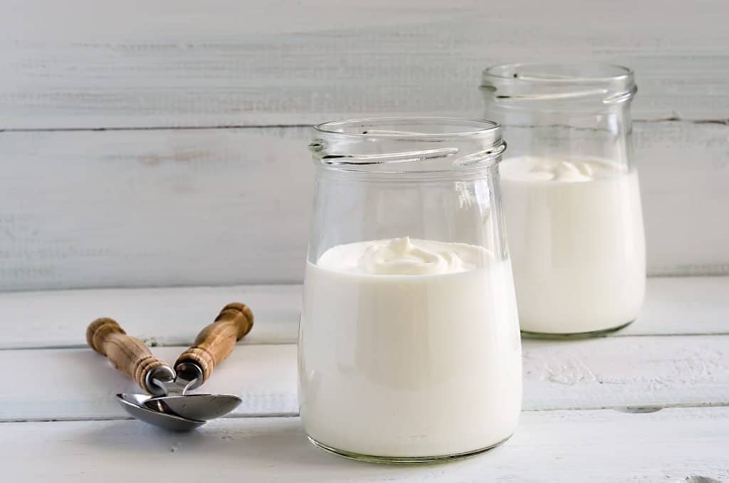 fresh yogurt in jars on wooden background with spoons