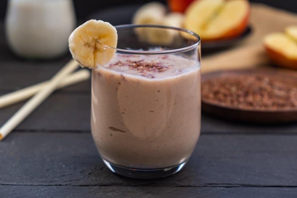banana smoothie in front of ingredients on dark wooden background