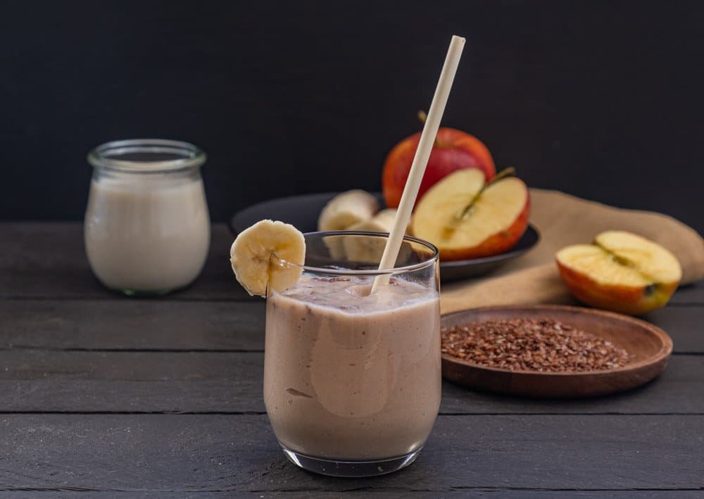 banana smoothie in front of ingredients on dark wooden background