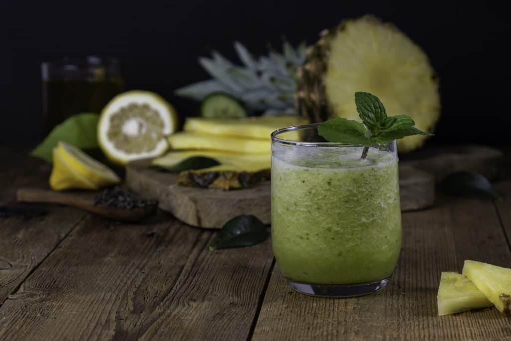 pineapple and cucumber detox smoothie in cup with ingredients in background