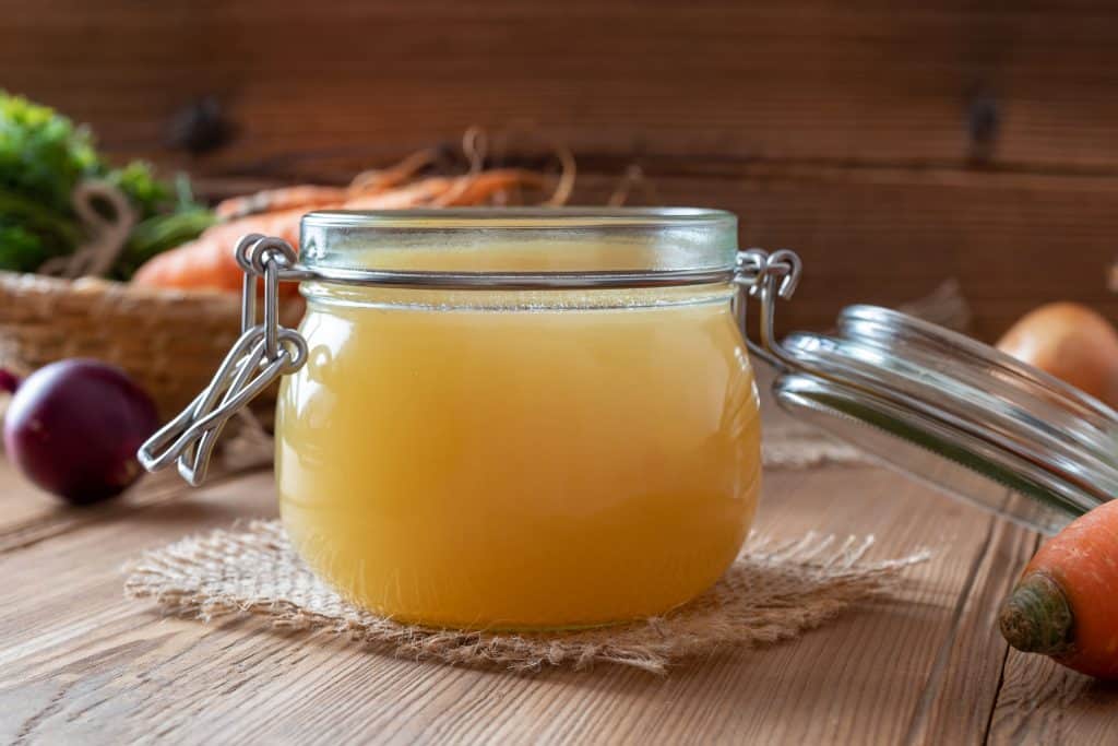 Chicken bone broth in a glass jar, with fresh vegetables in the background