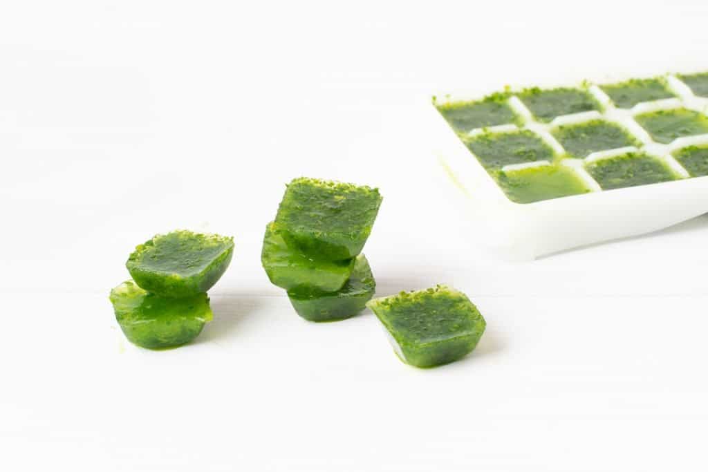 spinach ice cubes on a white table. frozen greens cubes.