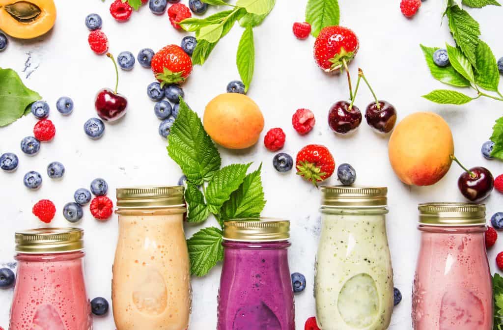 Healthy and useful colorful berry cokctalis, smoothies and milkshakes with yogurt, fresh fruit and berries on gray table