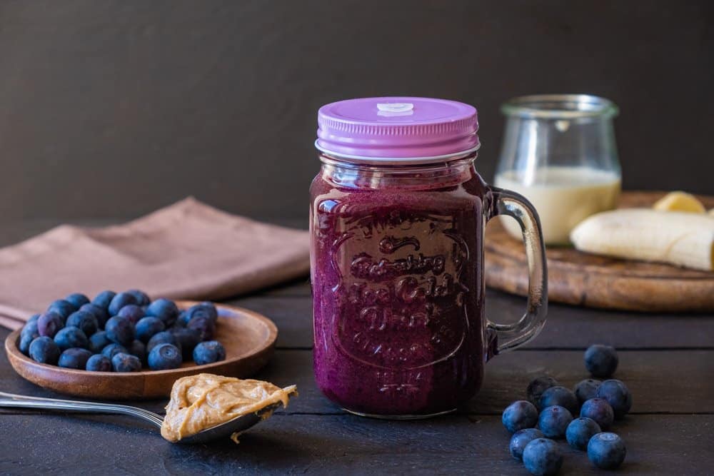 peanut butter blueberry smoothie in jar with ingredients in background