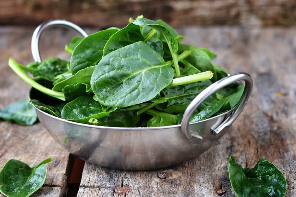 fresh baby spinach in a bowl on wooden background
