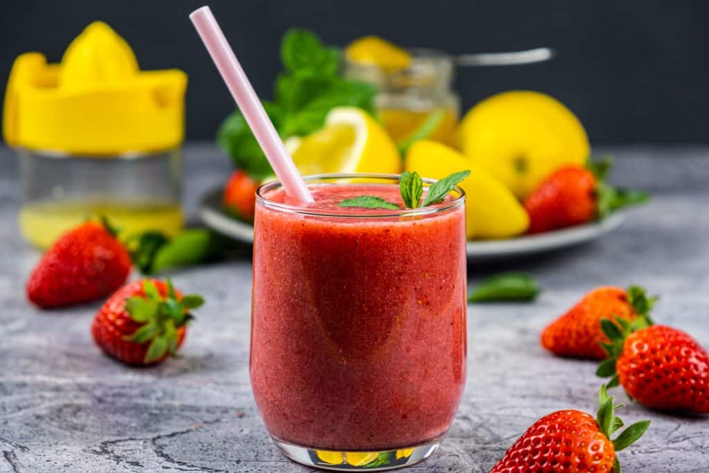 strawberry and lemon smoothie in glass with straw and ingredients in background