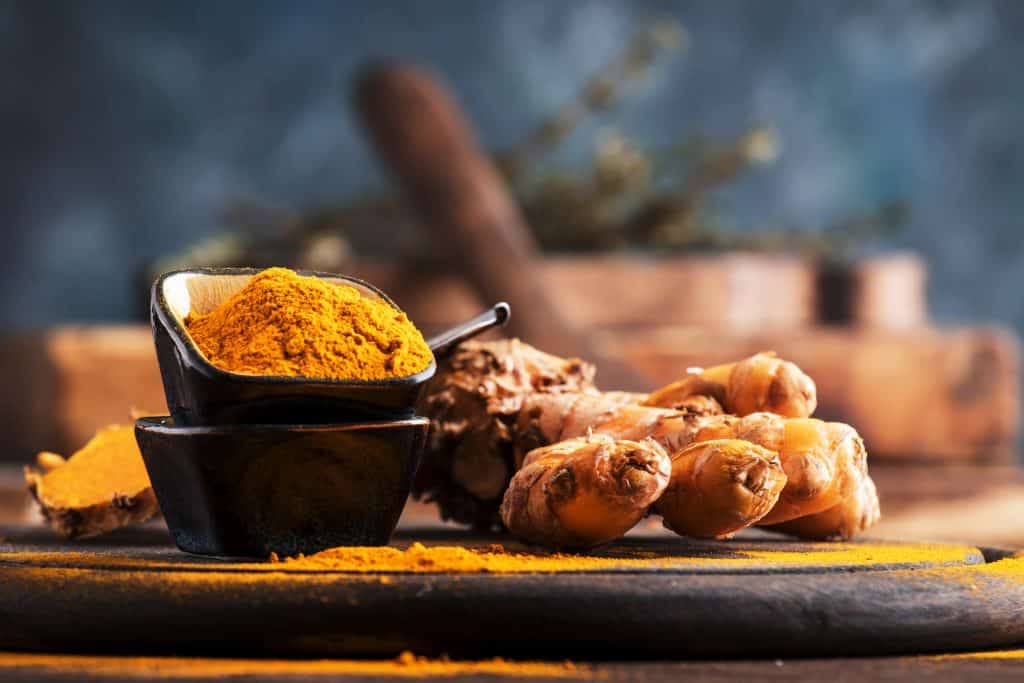 Turmeric powder and fresh turmeric on wooden background with copy space