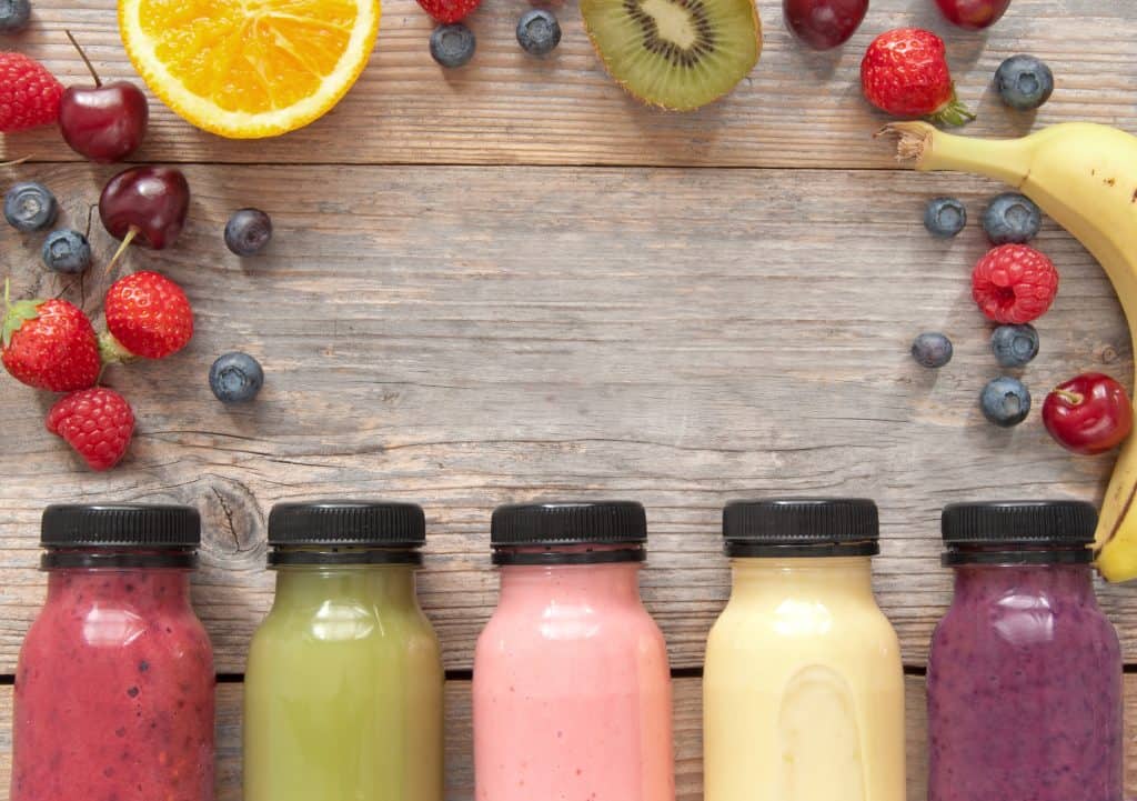 A variety of alkaline smoothies in bottles on wooden background with fruit