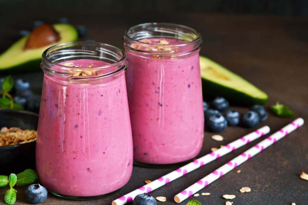 Smoothies of almond milk with avocado, flaxseed, banana, blueberries and granola on a dark background.