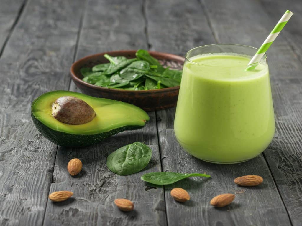 A drink of avocado, spinach and almond milk on a dark wooden table.