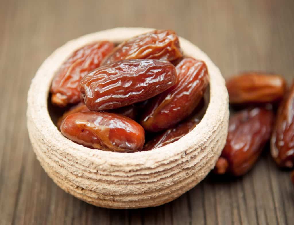 Delicious dates in small bowl on wooden surface