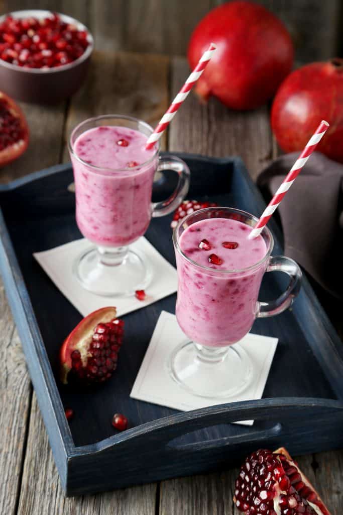 Pomegranate smoothie in glass and in tray on grey wooden background