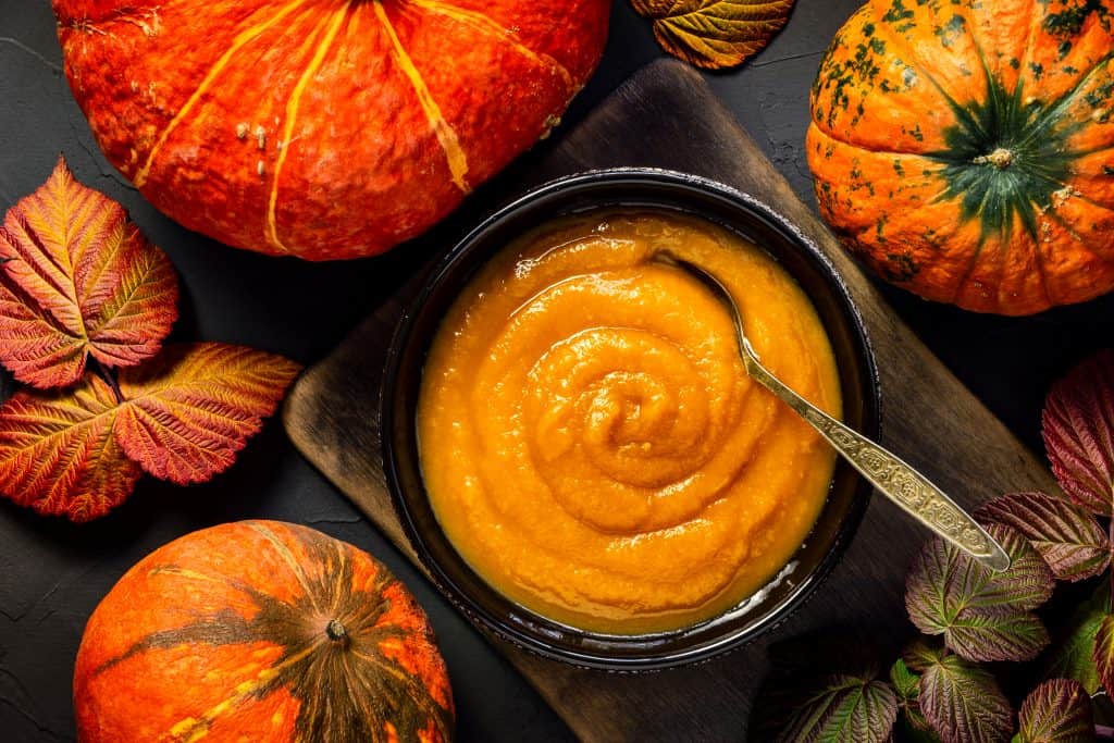pumpkin puree in bowl with spoon and pumpkins and leaves surrounding