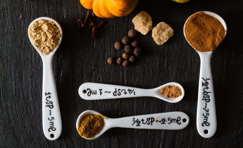 pumpkin pie spices in spoons on wooden background