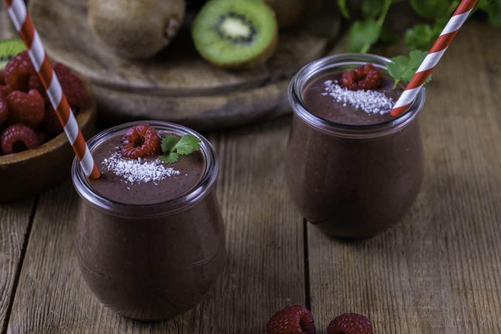 raspberry kale smoothies on wooden background with ingredients surrounding