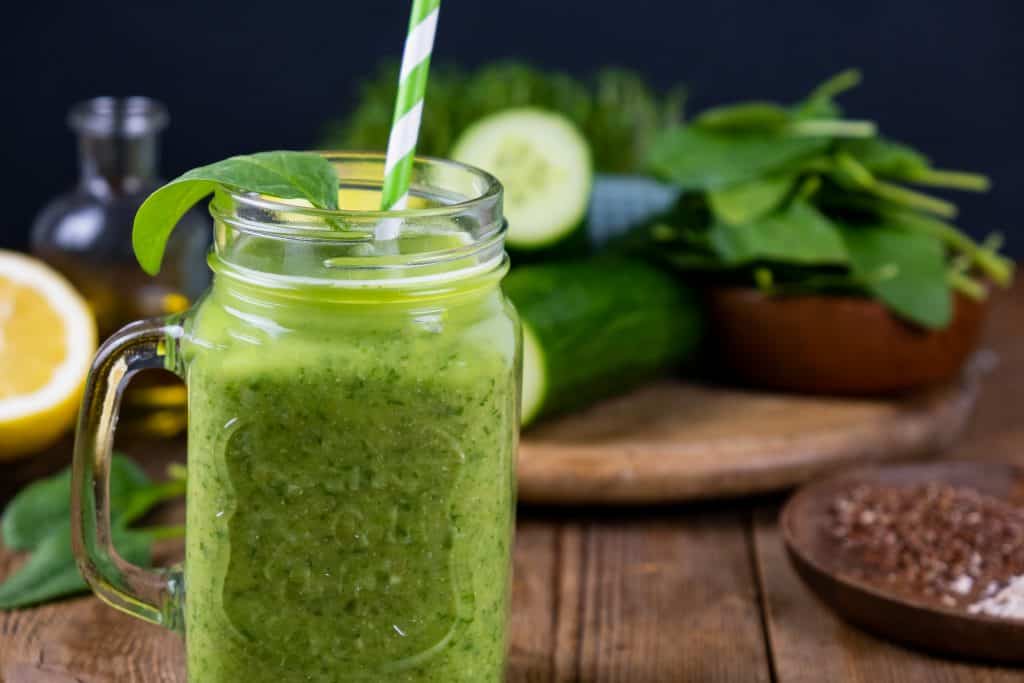 spinach oatmeal smoothie in glass on wooden background with ingredients