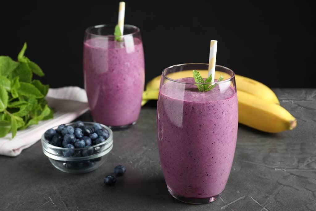 Glasses of delicious Greek yogurt smoothie for weight loss on grey table against black background