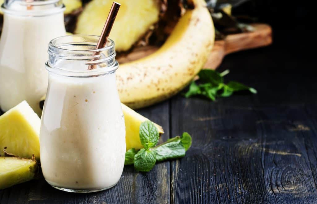 pineapple banana oat milk smoothie in two glasses on dark background