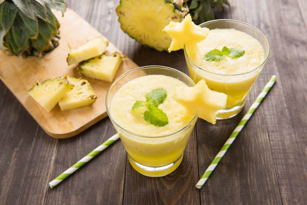 Pineapple smoothie with fresh pineapple on wooden table.