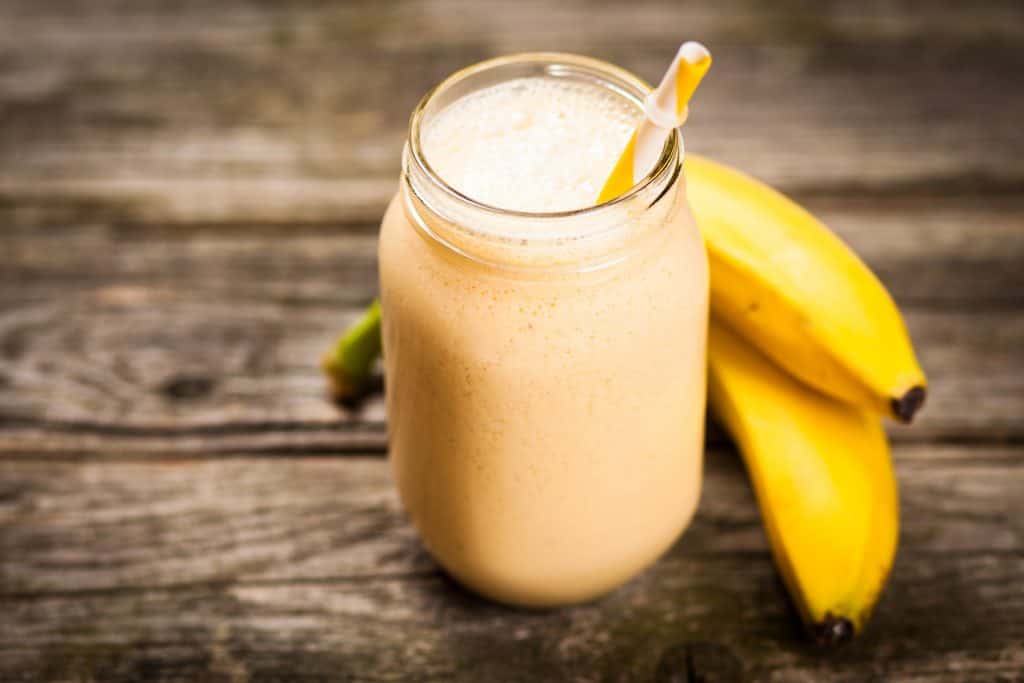 banana smoothie in glass on wooden table 