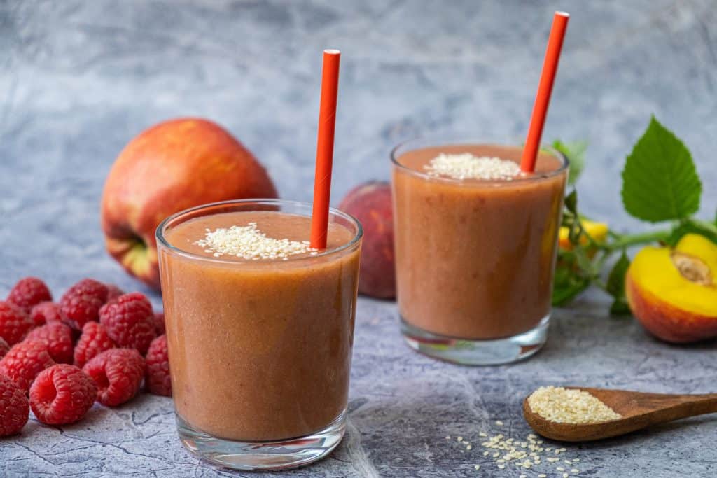 peach raspberry smoothies in glasses with ingredients around
