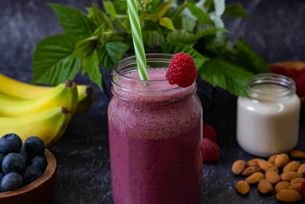 raspbery banana smoothie in glass with ingredients surrounding