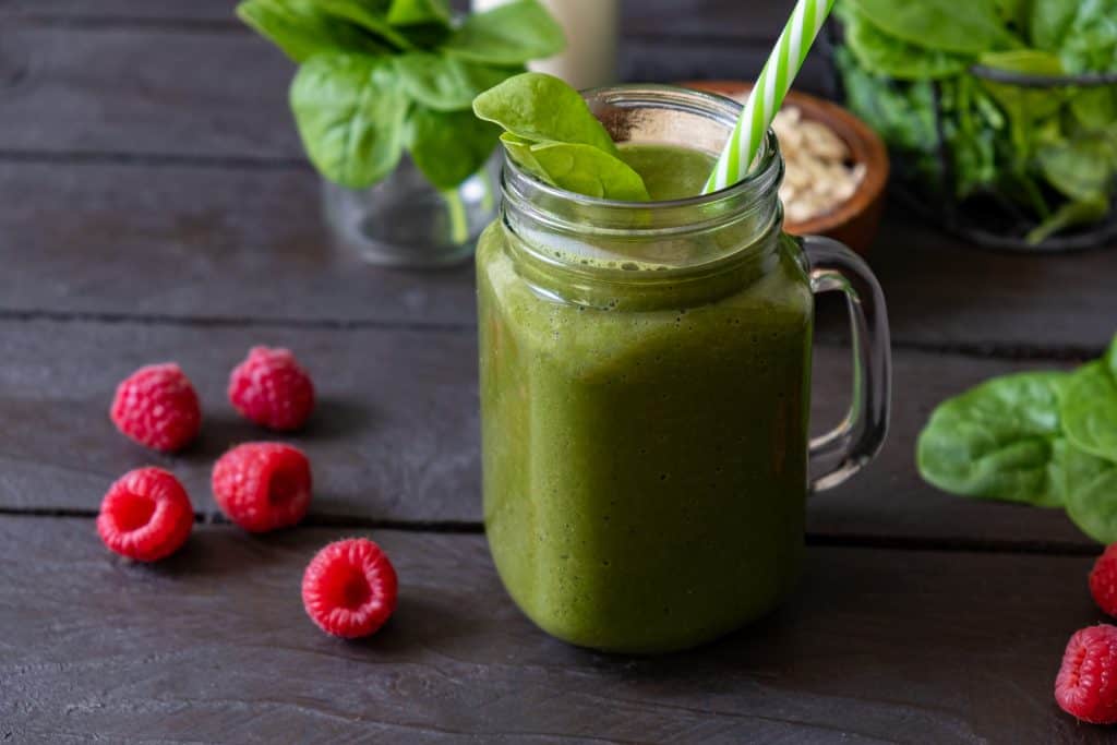 spinach raspberry smoothie in glass with ingredients surrounding