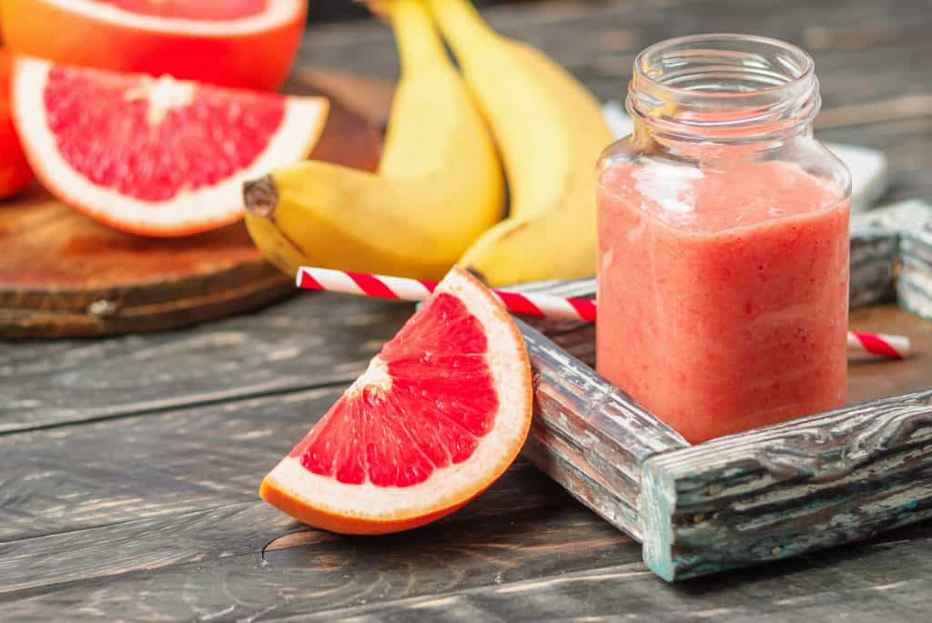 grapefruit banana smoothie in glass on wooden background with ingredients behind