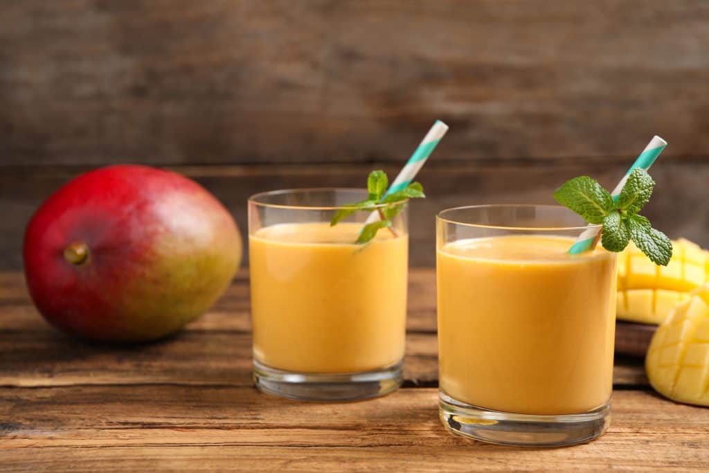 vegan mango smoothies in glasses with fresh mango in the background