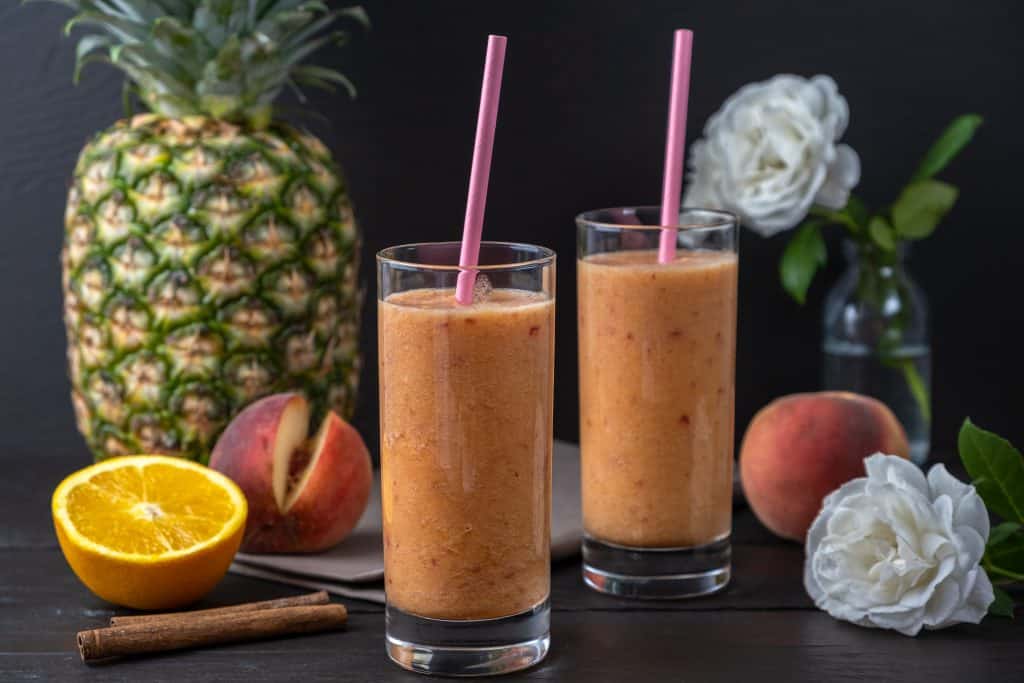 peach pineapple smoothies in glasses on dark background with ingredients surrounding