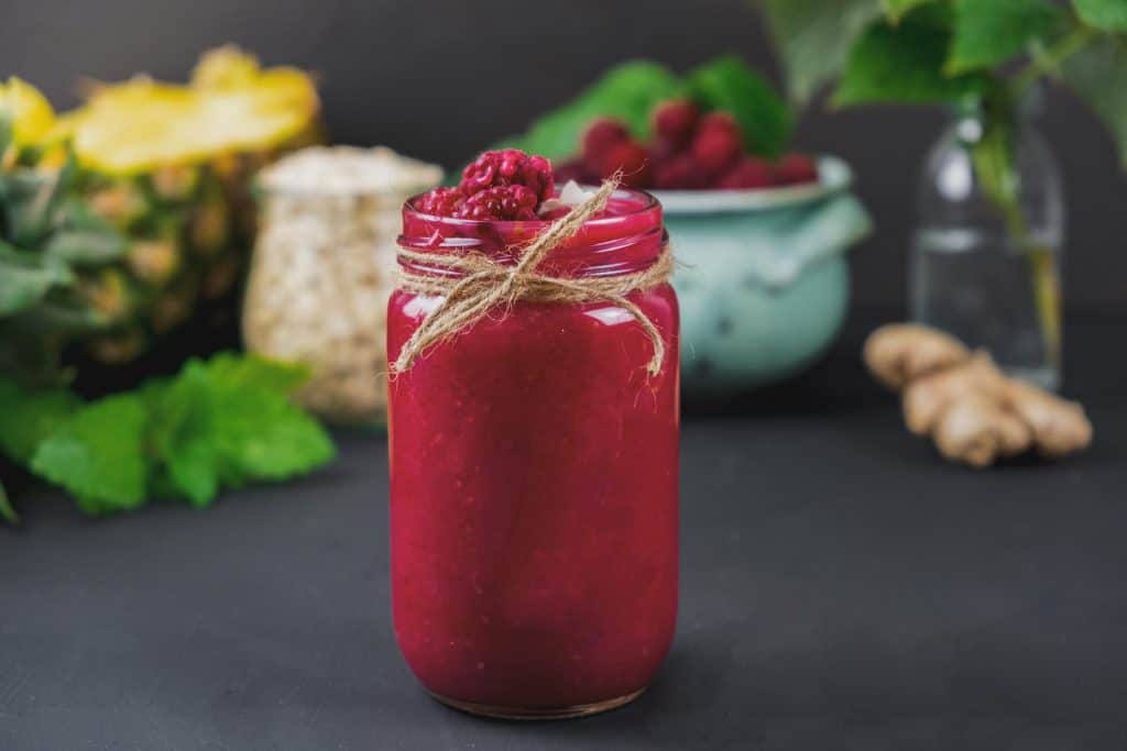 pineapple raspberry smoothie in glass with ingredients behind