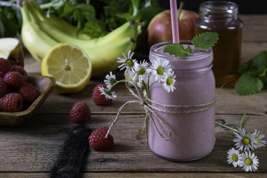 raspberry smoothie with banana in jar on wooden background with ingredients surrounding