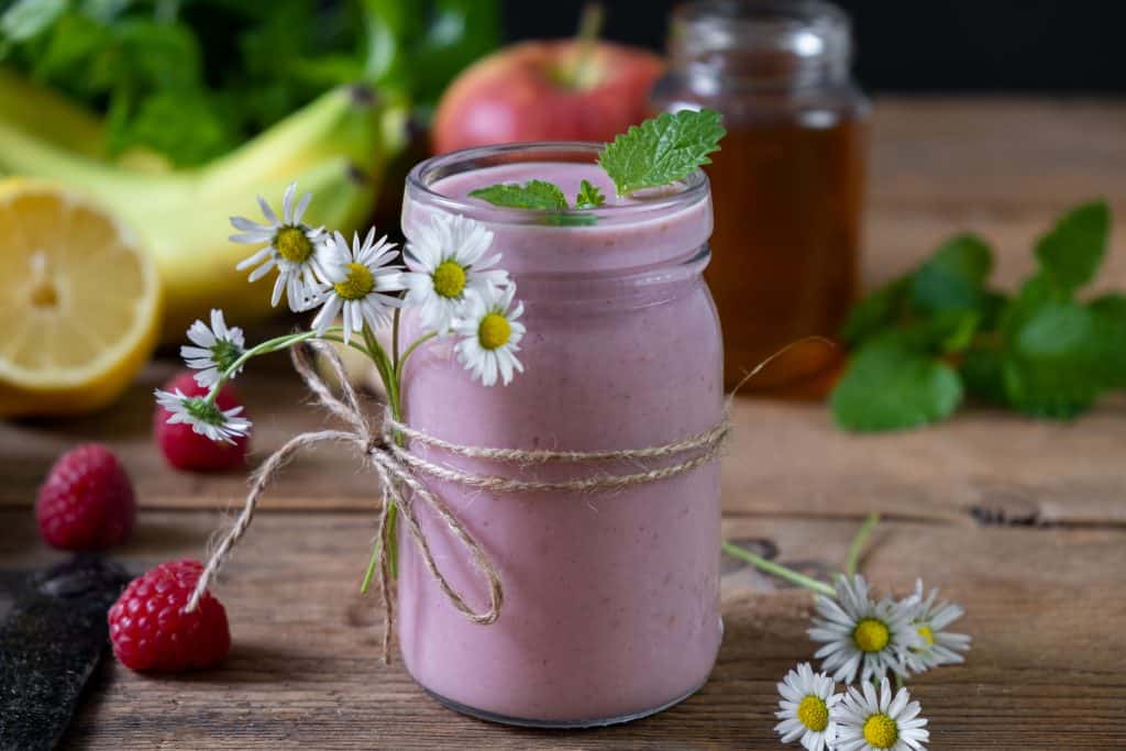 raspberry banana smoothie in jar with ingredients around on wooden background