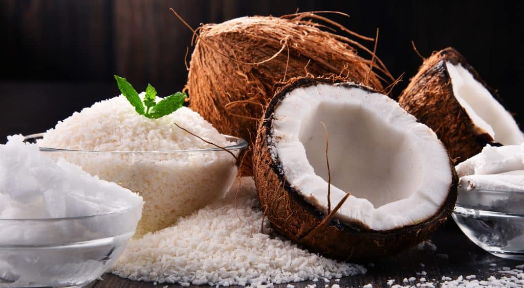 Composition with bowl of shredded coconut and shells on wooden table