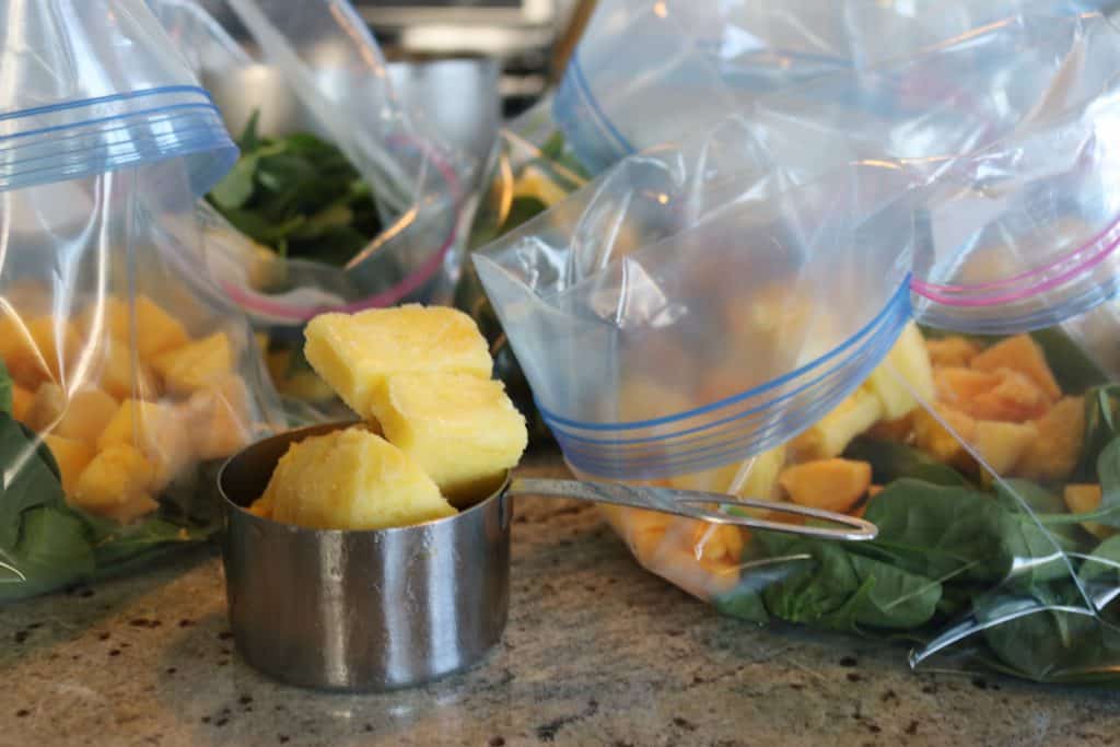 vegan smoothie bags being put together with spinach, mango and pineapple