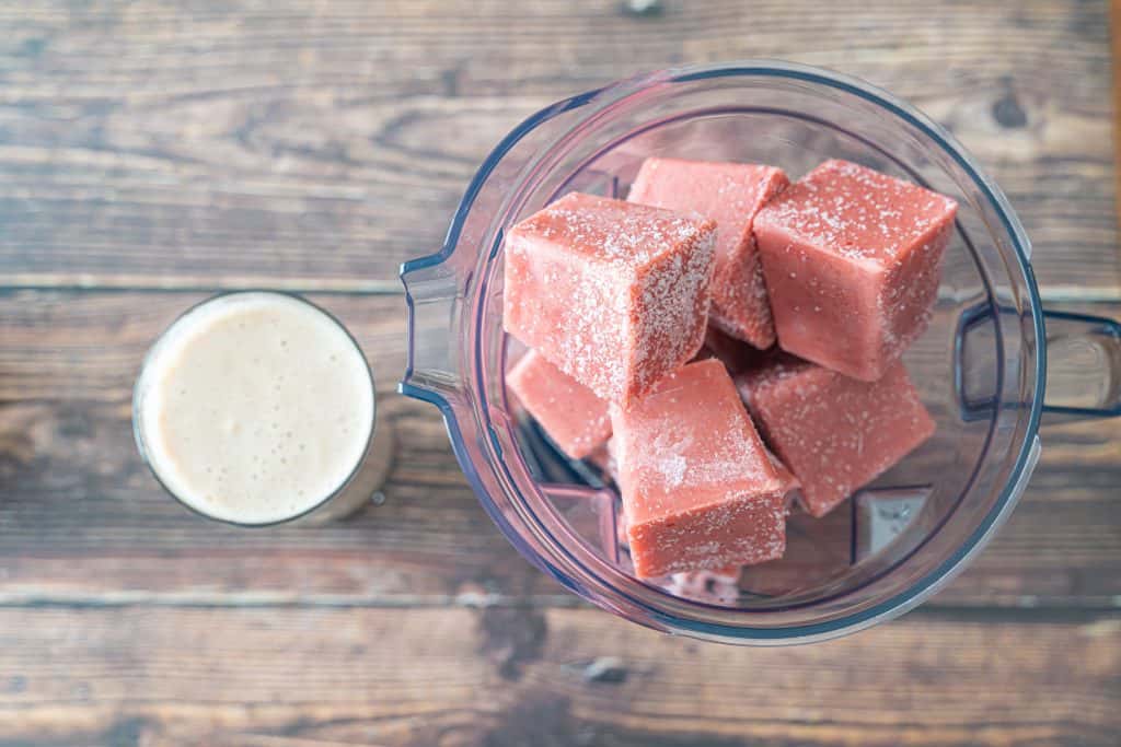 smoothie cubes in a blender with liquid in cup beside