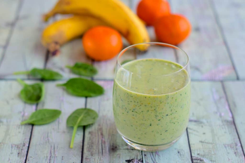 spinach orange smoothie in glass with ingredients behind