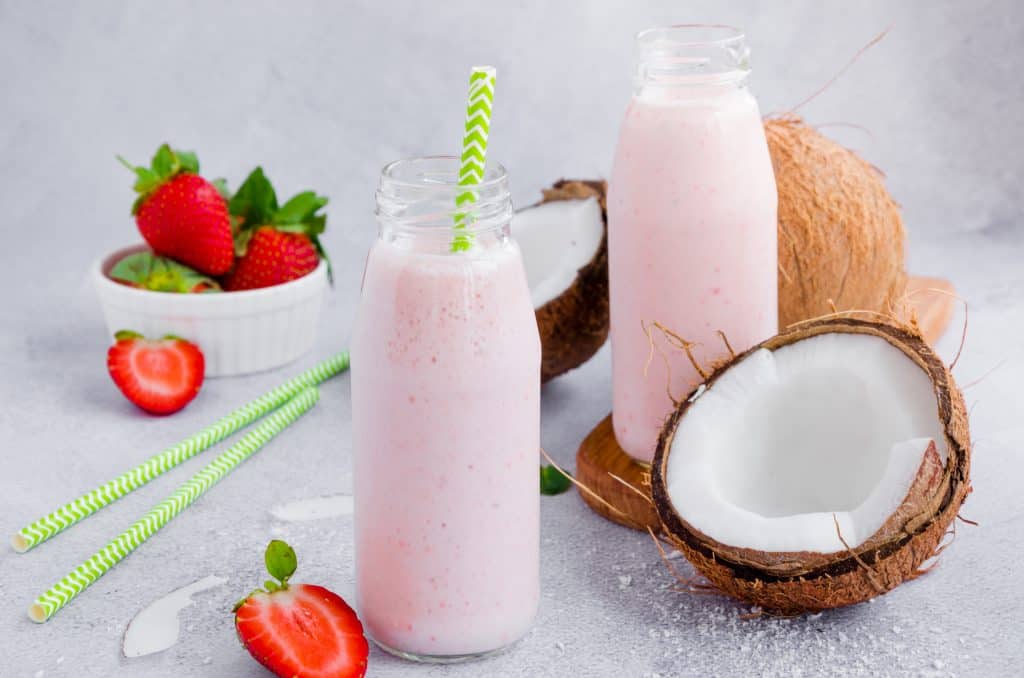 strawberry coconut cheesecake fat bomb smoothies on gray background with strawberries and coconut