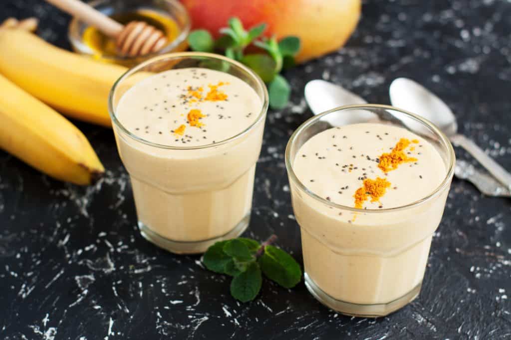 Tropical detox smoothies in glasses with banana, mango, turmeric and chia seeds