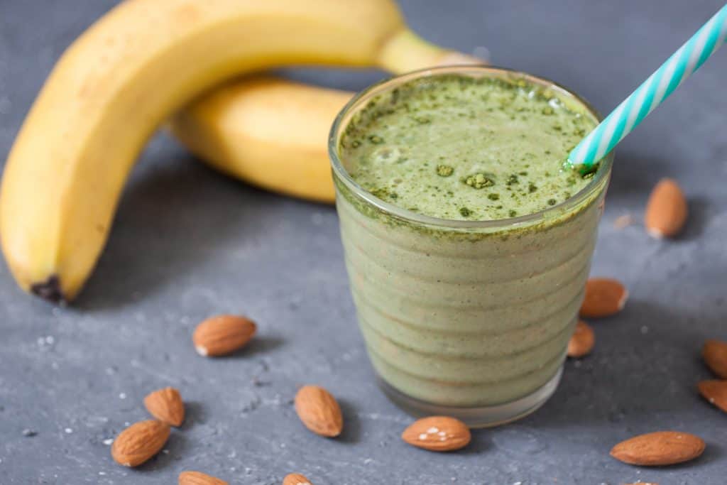 banana matcha smoothie in glass with bananas and almonds surrounding