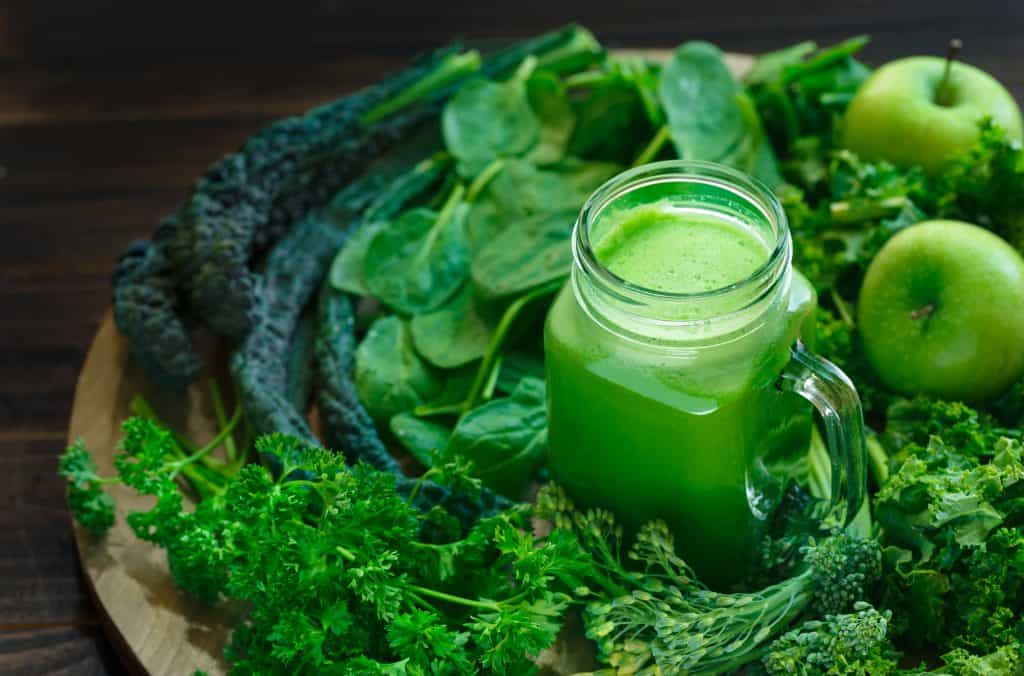 best greens for smoothies surrounding a green smoothie in mason jar