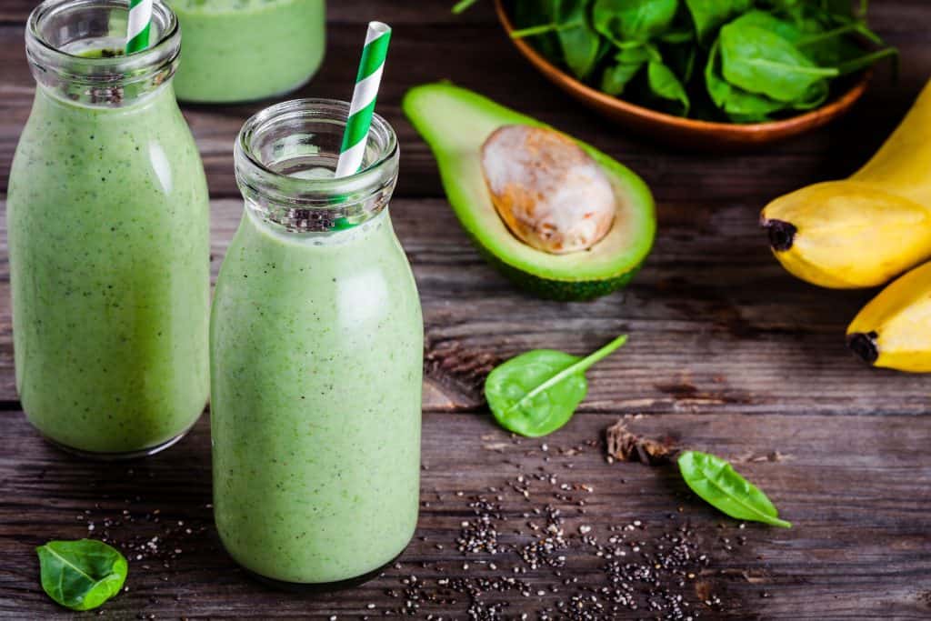 coconut water green smoothies in glass jars on wooden background with ingredients surrounding